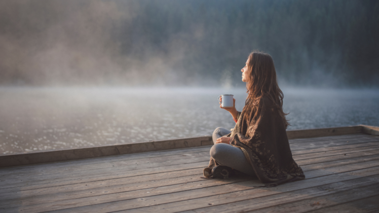 financial therapy client sitting by a peaceful lake with coffee, reflecting on her relationship with money and financial healing