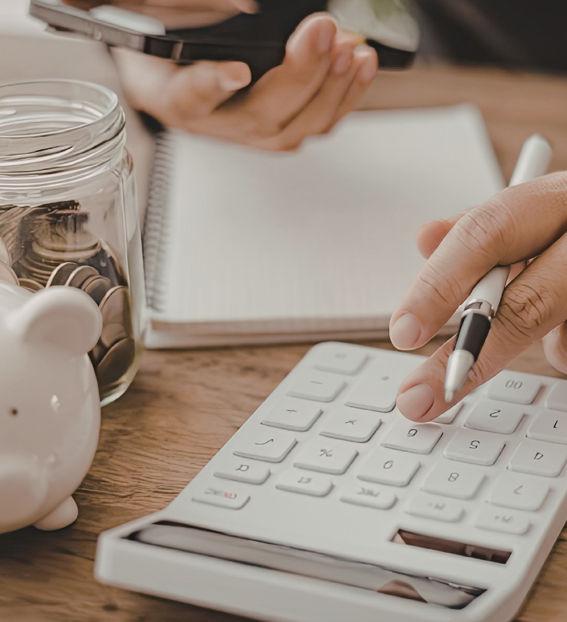 woman using a calculator with a piggy bank and jar of change nearby