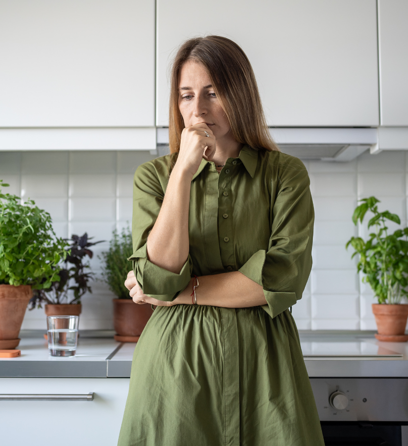 woman in a green dress thinking in her kitchen